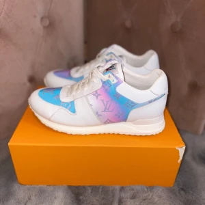 Louis Vuitton sneakers prism - Snygga Louis Vuitton sneakers i vitt skinn med prism i blått, rosa och lila. Skorna har LV-monogram över hela sidan och tån, samt vit sula och snörning. Perfekta för dig som vill sticka ut med exklusiv streetstyle.