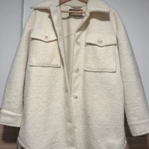 Vit overshirt i ullmix från New Yorker - Stilren vit overshirt från New Yorker i ullmix med klassisk krage, stora bröstfickor med lock och knäppning framtill. Jackan har en rak passform och långa ärmar, perfekt för lager-på-lager under kyliga dagar.