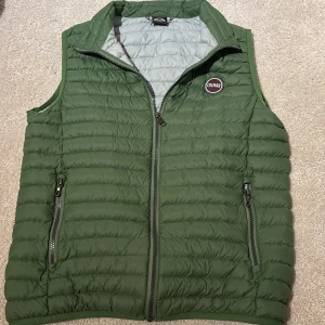 Grön colmarväst - Snygg grön dunväst från Colmar med quiltad design och dragkedja framtill. Västen har två praktiska fickor med dragkedja och en liten logga på bröstet. Perfekt att slänga över en hoodie eller tröja när det är kyligt ute.