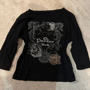 Svart topp med rosor från CPM Collection - Svart topp från CPM Collection med snyggt tryck och broderade rosor i grått och brunt framtill. Toppen har trekvartsärm och coola paljett- och kedjedetaljer som ger extra edge. Perfekt för dig som gillar unika detaljer och vill sticka ut. Man kan ha den som offshoulder-tröja, som på bilden, men det går att ha den vanligt också. Den är köpt på vinted och säljs pga att jag inte använder längre. Den är L men passar även mindre(jag är ca S)