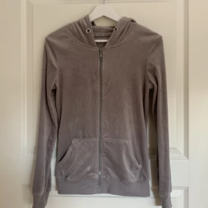 Beige hoodie med dragkedja - Mysig beige hoodie med dragkedja framtill och huva. Tröjan har två stora fickor och är gjord i ett mjukt, sammetsliknande material. Perfekt för chill dagar och enkel att matcha med det mesta. Långärmad och med ribbade muddar vid ärmslut och nederkant.