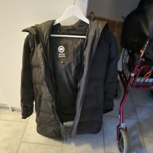 Canada Goose XS - Säljer en svart dunjacka från Canada Goose i storlek XS. Jackan har en fluffig pälskant på huvan, klassisk logga på ärmen och dragkedja framtill. Perfekt för kalla dagar med sin långa modell och varma dunfyllning. Säljer för använder inte den kvitto finns 