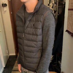 Grå dunväst från Polo Ralph Lauren - Hej! Säljer nu min as feta gråa dunväst från Polo Ralph Lauren. Fick den i present för ungefär ett halv år sen och den är i suverän skick. Den är i storlek M och nypris är runt 3600kr. Västen är perfekt nu till hösten så passa på att köp!  