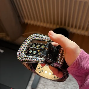 BB Simons Belt 100cm - Säljer ett svart bälte med massor av glittrande strass-stenar över hela remmen och spännet. Bältet har silverfärgade detaljer och en bred, rundad spänne som också är täckt av strass. Materialet är skinnimitation med metallkanter och hål för justering. 100cm långt