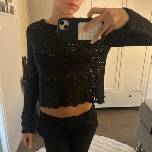 Svart virkad tröja - Svart virkad tröja med lång ärm och fin passform. Tröjan har ett snyggt hålmönster och vågig kant nertill, perfekt att styla med kostymbyxor eller en kjol. Lätt och luftig, passar när du vill ha en chill men ändå trendig look.