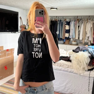 Svart t-shirt med vit text - Svart t-shirt med vit tryckt text på framsidan: 'I'M HOT U'RE NOT'. Modellen är kortärmad och har en avslappnad passform. Perfekt för dig som gillar statement-plagg och vill sticka ut lite extra. Materialet känns mjukt och skönt mot huden.