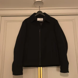 Svart jacka från Selected Homme - Stilren svart jacka från Selected Homme med klassisk krage och dragkedja framtill. Jackan har en rak passform, långa ärmar med knappdetalj vid ärmslut. Perfekt för hösten🍁🍂 fråga mig om du har några frågor Mvh/Max