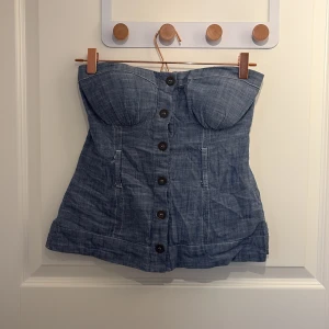 Korsetttopp - Cool topp med jeans liknande tyg. Går att öppna framtill och har vadderade kupor. Storlek S. Köpt second hand men originellt från bebe. Använd enstaka gång men bra skick, gissar dock att det fattas ett skärp till men är lika snyggt utan❤️