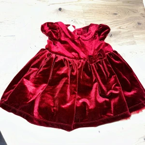 Vinröd sammetsklänning från H&M julklänning  - En söt, röd klänning med sammetsliknande yta. Den har en krage och puffärmar, samt en liten rosett på midjan. Klänningen har en utställd kjol med tyll underkjol och knäpps med knappar i ryggen. Supersöt vinröd klänning i mjuk sammet från H&M med puffärmar, rund krage och dekorativ rosett i midjan. Klänningen har knappar i ryggen och ett lager av tyll under kjolen för extra volym. Perfekt för dig som gillar lite extra glam. Gör alla tillfällen - jul - födelsedag 🎁- fest 🎈 