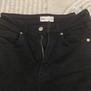 Svarta bootcut jeans från Zara, strl 36 - Svarta jeans från Zara i storlek 36 med klassisk femficksdesign, dragkedja och knapp framtill. Byxorna har bootcut-modell med lätt utsvängda ben och är tillverkade i ett mjukt jeanstyg. Perfekta för en trendig och avslappnad look.