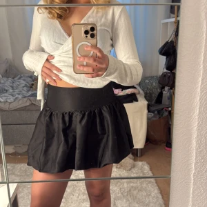 Svart kortkjol med volym - Säljer en svart kortkjol med bred midjeresår och voluminös, lätt utställd form. Kjolen har en enkel och stilren look som är lätt att matcha. Perfekt för dig som gillar en feminin och trendig stil.