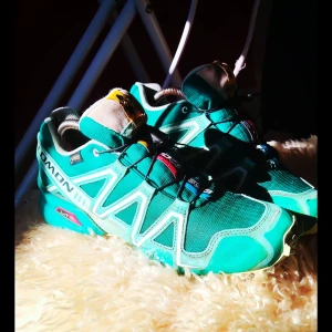 Turkosa Salomon Speedcross Sneakers/Löparskor [40] - Säljer ett par turkosa Salomon Speedcross sneakers med GORE-TEX och snabbsnörning. Skorna har grov sula med bra grepp, detaljer i vitt och grått samt LT-märkning på sidan. Perfekta för utomhusaktiviteter och träning. Finns en liten missfärgning i tyget annars i kanonskick som ni ser. 
