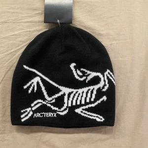 Svart mössa från Arc'teryx - Svart stickad mössa från Arc'teryx med stor vit logga och broderad Arc'teryx-text framtill. Helt ny och aldrig använd. Skickar inom 1-3 dagar.