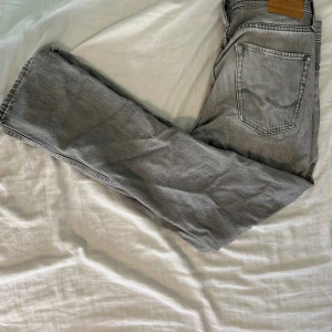 Grå jeans från Jack & Jones - Snygga grå jeans från Jack & Jones med klassisk femficksdesign och ljus tvätt. Jeansen har en rak passform och är tillverkade i mjukt bomullsmaterial. Detaljer som fransad kant vid benslut ger en cool och avslappnad vibe.