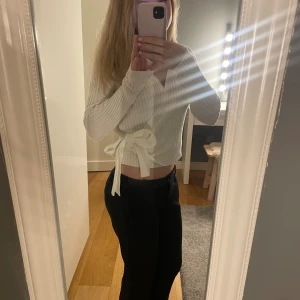 Vit omlott kofta med knyt - Säljer en superfin vit omlott kofta med ribbad struktur och knyt i sidan. Tröjan är croppad, har lång ärm och v-ringad hals. Perfekt att styla med både jeans och kjol för en trendig look.