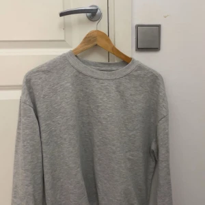 Grå basic sweatshirt i bomull - Enkel och stilren grå sweatshirt med rund halsringning och långa ärmar. Tröjan är tillverkad i mjuk bomull och har en relaxed passform, perfekt för chill dagar eller när du vill ha en clean look.