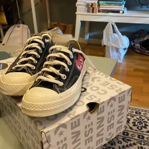 Converse Play Comme des Garçons sneakers - Svarta Converse Play Comme des Garçons sneakers med den ikoniska röda hjärtloggan på sidan. Klassisk låg modell med vita snören, vit tå och sula. Skorna är i canvas och har en platt sula och rund tå. Perfekta för dig som gillar streetstyle och vill sticka ut.
