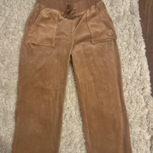 Beiga mjukisbyxor Juicy Couture S - Mysiga beiga mjukisbyxor från Juicy Couture. Byxorna har stora fickor fram och bak med tryckknappar och broderad logga på ena fickan. Har en liten skada vid fickan men använt max 1 gång.                Byxorna storlek: S Koftan storlek: M