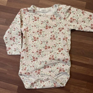 Blommig body - Långärmad body från Newbie i storlek 62 (2-4mån). Sparsamt använd utan anmärkningar. Knäppning vid axel och gren.