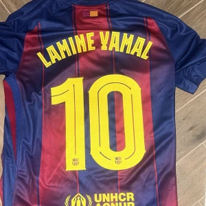 FC Barcelona Lamine Yamal tröja Nike M - Säljer en officiell FC Barcelona matchtröja med Lamine Yamal och nummer 10 på ryggen. Tröjan är kortärmad, har blå och röda vertikala ränder, gula detaljer och klubbmärke på bröstet. Materialet är lätt och andas, perfekt för fotboll. Champions League-märke på ärmen.   Äkta och köpt i barcelona i fan butiken. Säljs då den inte passar mig. Pris går att diskuteras.