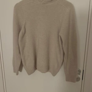 Beige polotröja från Gran Sasso - Mysig beige polotröja från Gran Sasso, tillverkad i Italien. Tröjan har lång ärm, ribbade muddar och en hög polokrage som ger en chill och stilren look. Perfekt för lager på lager under kyliga dagar.