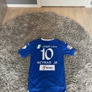 Blå Al Hilal Neymar Jr fotbollströja Puma - Säljer en blå Al Hilal fotbollströja med Neymar Jr och nummer 10 på ryggen. Tröjan har vita detaljer, tryckta sponsorer och klubbmärke framtill. Tillverkad i lätt och ventilerande material, perfekt för match eller träning. Obs tröjan är fejk igen riktigt.! Strorlek S/m passar båda