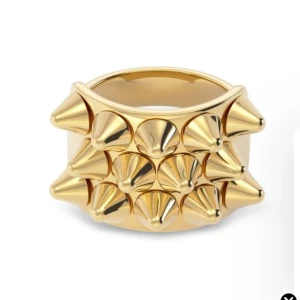 Edblad peak ring - Cool och chunky guldfärgad ring med flera spetsiga nitar på framsidan. Ringen har en bred form och ger en edgy vibe, perfekt för dig som gillar att sticka ut med dina accessoarer.