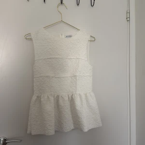 Vit blus från WERA - Säljer en jättefin vit blus från WERA med ärmlös design och volang nedtill