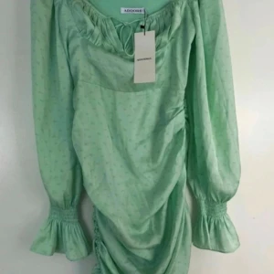 Mintgrön klänning från Adoore - Superfin mintgrön klänning från Adoore med långa puffärmar och smock vid ärmsluten. Klänningen har knytning vid halsen och lätt rynkade partier längs kjolen. Tunt, flowigt material med diskret mönster.