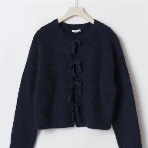 Mörkblå kofta med rosettknäppning - Superfin mörkblå kofta med lång ärm och rund hals. Koftan är stickad och har unika rosetter som knäppning framtill, vilket ger en söt och trendig look. Perfekt att slänga över en topp när det är kyligt ute. Säljer för den bara legat i garderoben, ingen användning alls💗