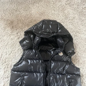 Svart dunväst från Moncler med luva - Jag säljer då min Moncler väst för jag använder den inte längre den är i jätte bra skick och storlek S/1. Det ändå som är felet men västen är dragkedjan som är borta med den funkar fortfarande