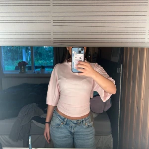 Ljusrosa omlottopp från Gina Tricot - Säljer en ljusrosa omlottopp från Gina Tricot i mjukt och stretchigt material. Toppen har trekvartsärmar och en snygg knytning i ryggen som ger en cool detalj. Passformen är normal och toppen är croppad, perfekt till jeans eller kjol.