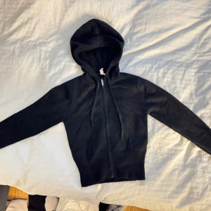 Svart stickad hoodie från Nelly - Svart stickad hoodie från Nelly med dragkedja framtill och snörning i huvan. Tröjan har långa ärmar och bred ribbad mudd vid midjan.  Aldrig använd, skickas samma dag och mer bilder kan ordnas Mvh!