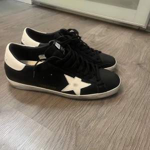 Golden Goose  - Golden Goose sneakers i svart skinn med vit häl och ikonisk vit stjärna på sidan. Dom är storlek 46 och helt oanvända. 