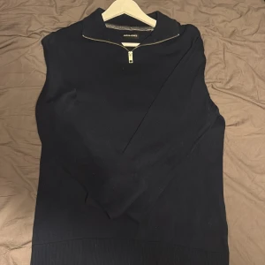 Mörkblå half zip tröja Jack & Jones - Mörkblå långärmad tröja från Jack & Jones med stilren half zip-dragkedja vid kragen. Tröjan har en klassisk passform och är tillverkad i mjukt material som passar perfekt till lager-på-lager. Enkel och snygg design utan mönster.