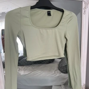 Ljusgrön croppad topp  - Säljer en ljusgrön croppad topp med lång ärm och fyrkantig ringning. Toppen är ribbad och har en tight passform som framhäver siluetten. Perfekt för dig som gillar stilrena och trendiga plagg.