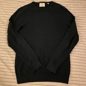 Mörkblå stickad tröja från Black - En stilren mörkblå stickad tröja från Black i storlek S. Tröjan har rund halsringning och långa ärmar med ribbade muddar vid ärmslut och nederkant. Perfekt för dig som gillar enkel och clean look.