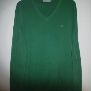Grön v-ringad tröja från J.Lindeberg - Snygg grön v-ringad tröja från J.Lindeberg med diskret logga på bröstet. Tröjan har lång ärm och är tillverkad i mjukt material som känns skönt mot huden. Perfekt för dig som gillar stilrena och klassiska plagg.