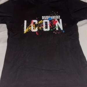 Svart Dsquared2 ICON t-shirt - Svart t-shirt från Dsquared2 med stort vitt 'ICON'-tryck och färgglada färgstänk över bröstet. Klassisk passform och rund hals. Perfekt statement-plagg för dig som vill sticka ut.