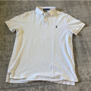 Vit pikétröja från Polo Ralph Lauren - Vit pikétröja från Polo Ralph Lauren i custom slim fit. Klassisk krage, korta ärmar och broderad logga på bröstet. Tillverkad i mjuk bomull, perfekt för en clean och stilren look.