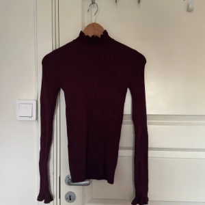 Vinröd ribbad polotröja Gina Tricot XS - Vinröd ribbad polotröja från Gina Tricot i storlek XS. Tröjan har lång ärm, tight passform och en hög krage med volangkant. Perfekt till lager-på-lager och snygg till både jeans och kjol.