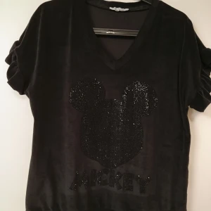 Svarta mjukisbyxor i sammet - Svarta mjukisbyxor i mjuk sammet med relaxed fit. Byxorna har resår i midjan och är perfekta för chill dagar. Matchar toppen med glittrig Mickey Mouse-detalj om du vill köra hela setet.