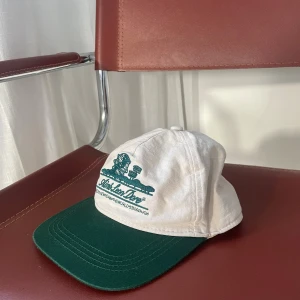 Aimé Leon Dore ‘World’s Borough’ Cap – White/Green Edition  - Storlek: Justerbar / One Size   Skick: Mycket fin, endast använd ett fåtal gånger   Beskrivning: Exklusiv Aimé Leon Dore-keps i vitt med grönt broderad "Queens, New York - The World's Borough"-logotyp framtill. Ett rent och eftertraktat plagg, tack vare den otroligt bra passformen. Justerbar rem baktill för perfekt passform. Nypris 1200 på StockX.