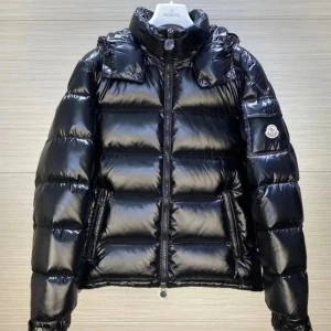 Svart pufferjacka från Moncler - Snygg svart pufferjacka från Moncler med glansig finish och klassisk logga på ärmen. Jackan har hög krage, dragkedja framtill och två fickor med dragkedja. Perfekt för kalla dagar när du vill hålla stilen.