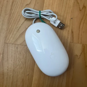 Apple Mighty Mouse (A1152) - Apple Mighty Mouse med USB-anslutning, modell A1152. Klassisk vit design med rullkula och optisk sensor. Fungerar med Mac och PC. Mindre repor och normalt slitage syns, men i gott skick. Perfekt för samlare eller som reservmus.