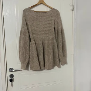Beige stickad tröja från SHEIN - Beige stickad tröja från SHEIN i storlek M. Tröjan har långärmade ballongärmar, rund hals och ett ribbat midjeparti som ger en snygg peplum-effekt. Materialet är 100% polyester och den har en mjuk, grovstickad struktur som känns cozy och trendig.