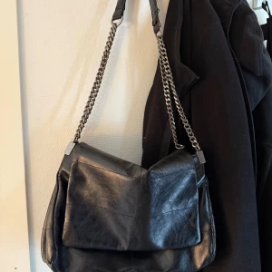 Svart axelväska i skinn med kedja - Snygg svart axelväska i mjukt skinn med grov silverfärgad kedja som axelrem. 