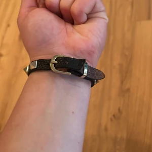 Svart läderarmband med nitar - Coolt svart armband i läder med silvriga pyramidformade nitar runt om. Spännet är i metall och ger en snygg kontrast mot det svarta lädret. Perfekt accessoar för att ge din outfit en edgy vibe.