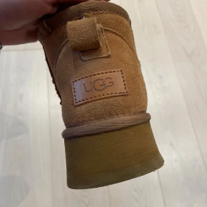 UGG boots i mocka med päls, strl 37 - Säljer ett par klassiska real UGGs i brun mocka med fluffigt vitt pälsfoder. Endast använda ungefär 7 gånger då jag egentligen vill ha lägre sula. Fortfarande fluffiga inuti! En av skorna har en liten missfärgning, men det är absolut inget man tänker på! 
