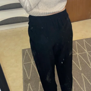 Svarta byxor med knyt i midjan från 157 - Svarta byxor från 157 i storlek S. De har hög midja med elastisk resår och ett snyggt knytband framtill. Byxorna har en rak och lite lösare passform, perfekta för en chill och stilren look. Materialet känns mjukt och lätt, vilket gör dem sköna att bära hela dagen.